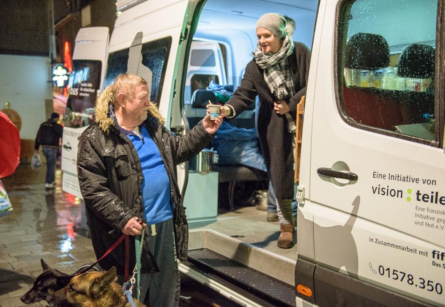 Ein Mann mit zwei Hunden steht vor dem gutenachtbus in Düsseldorf und nimmt ein Getränk entgegen.