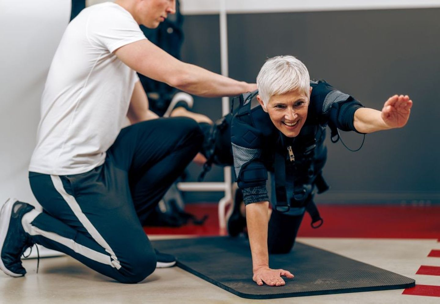 EMS-Training: Eine Seniorin führt eine Sportübung nach Anleitung ihres Trainers aus.