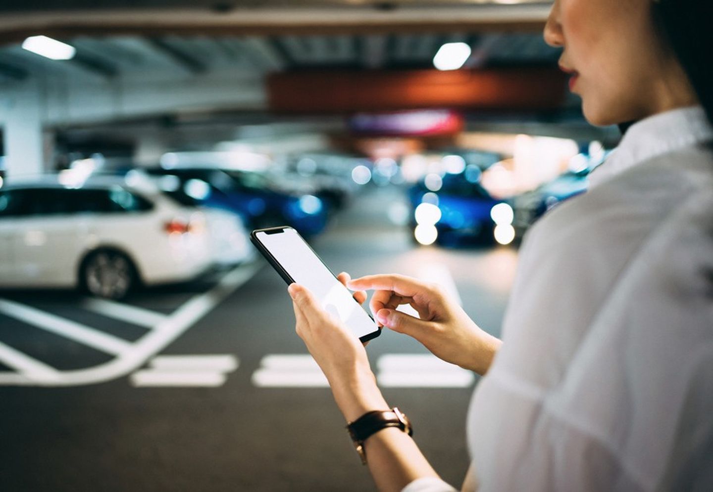 Mobilität der Zukunft: Eine Frau checkt ihr Smartphone, bevor sie zu ihrem Auto geht.