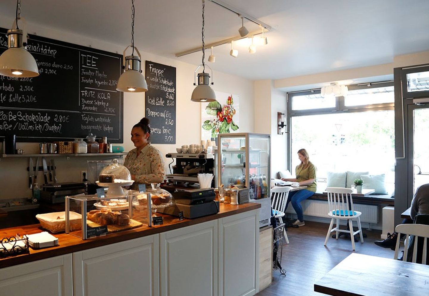 Eine Baristarei mit großer Holztheke, hinter der Mitarbeiter stehen. Es sitzen ein paar Gäste an den Tischen.