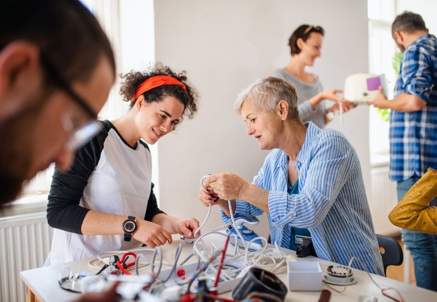 Eine Gruppe von Personen unterschiedlichen Alters widmet sich der Reparatur verschiedener Geräte. © Halfpoint Images / Moment via Getty Images 