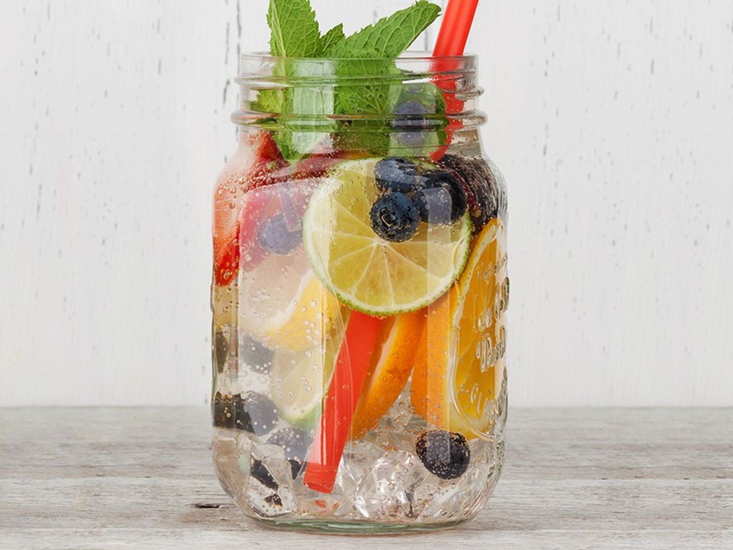 Ein Glas Vitaminwasser mit Blaubeeren, Orangen, Zitronen, Minzblättern und Eiswürfeln.