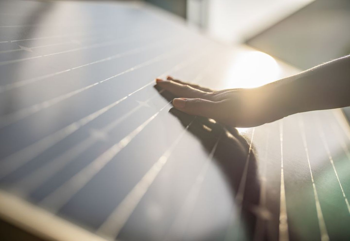 Eine Hand streicht über ein Solarmodul, auf das Sonne scheint. © Witthaya Prasongsin / Moment via Getty Images