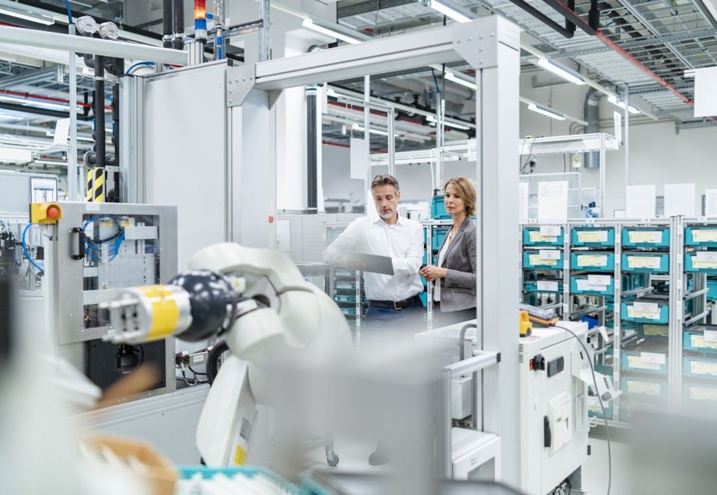 Eine Frau und ein Mann mit einem Tablet in der Hand stehen in einer modernen Industriehalle mit diversen Maschinen. © Westend61 / Westend61 via Getty Images