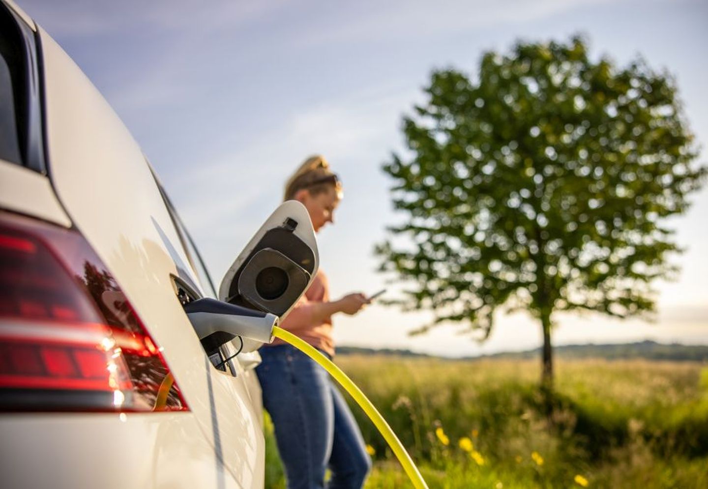Eine Frau lädt ihr E-Auto am Rand einer Wiese. © SimonSkafar / E+ via Getty Images