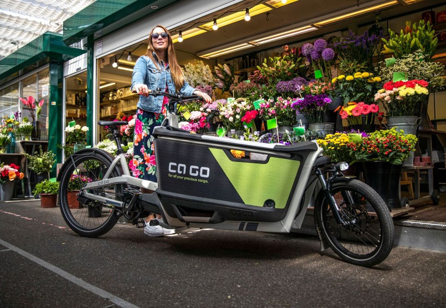 Eine Frau steht mit ihrem E-Lastenrad vor einer Blumenhandlung. 