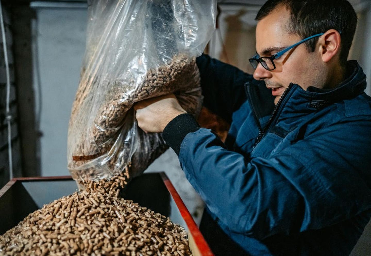 Pelletheizung: Ein Mann befüllt einen Pelletkessel manuell mit Pellets.