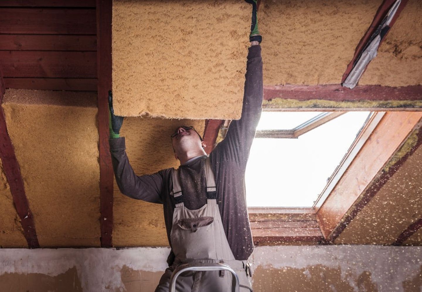 Energetische Sanierung: Mann steht auf einer Leiter und dämmt das Dach eines Hauses.