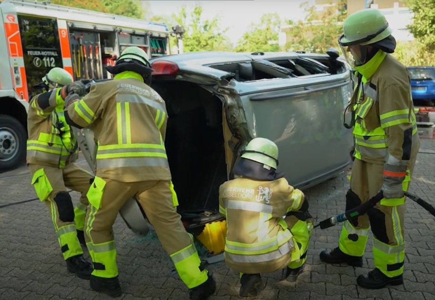 Schüler:innen der Feuerwehrschule Düsseldorf schneiden auf einem Übungsplatz der Feuerwehr ein verunfalltes Fahrzeug von der Dachseite auf.