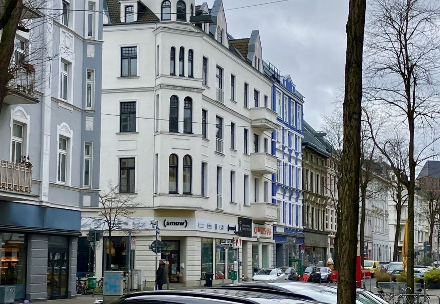 Blick auf eine Straße mit Altbauten und parkenden Autos. 