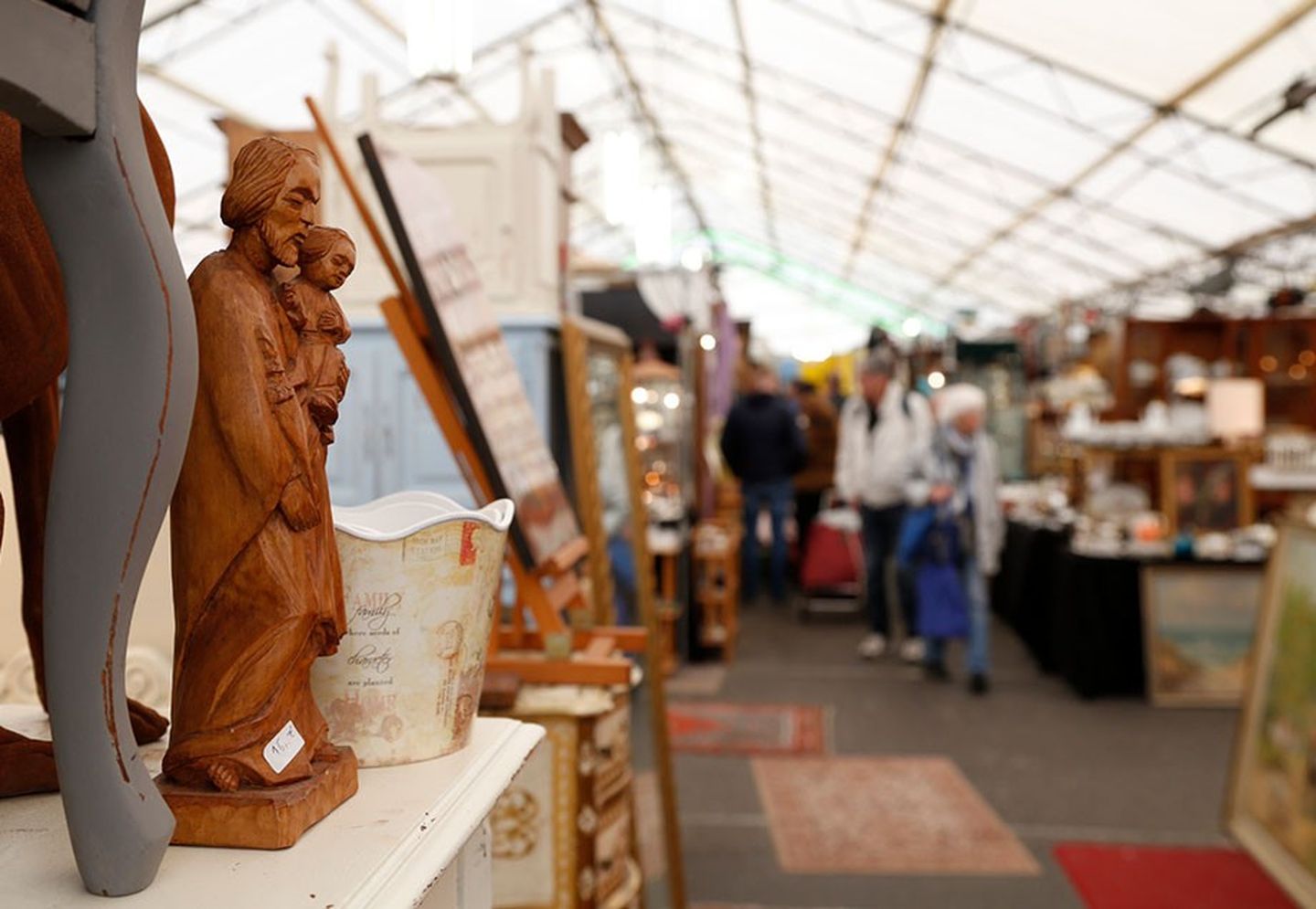 Eine Trödelmarkthalle mit alten Figuren, Möbeln und verschwommenen Besuchern im Hintergrund.