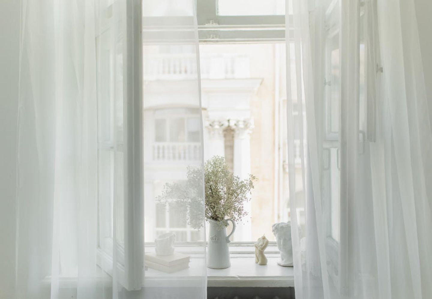 Richtig Lüften gegen Schimmel: Ein helles Zimmer mit transparenten Vorhängen und einem offenen Fenster.