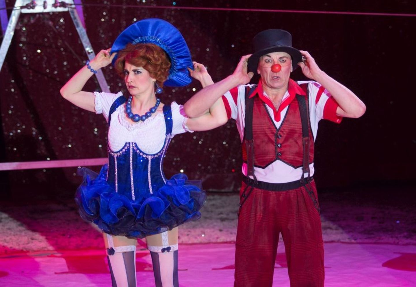 Ein Clown und seine kostümierte Assistentin heben ihre Arme zu den Köpfen verziehen die Gesichter zu erstaunten Grimassen.