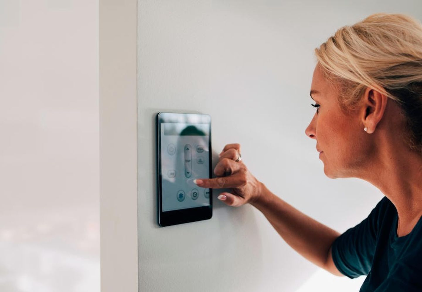 Eine Frau, die die Innentemperatur ihres Hauses mit Hilfe eines Tablets an der Wand reguliert. 