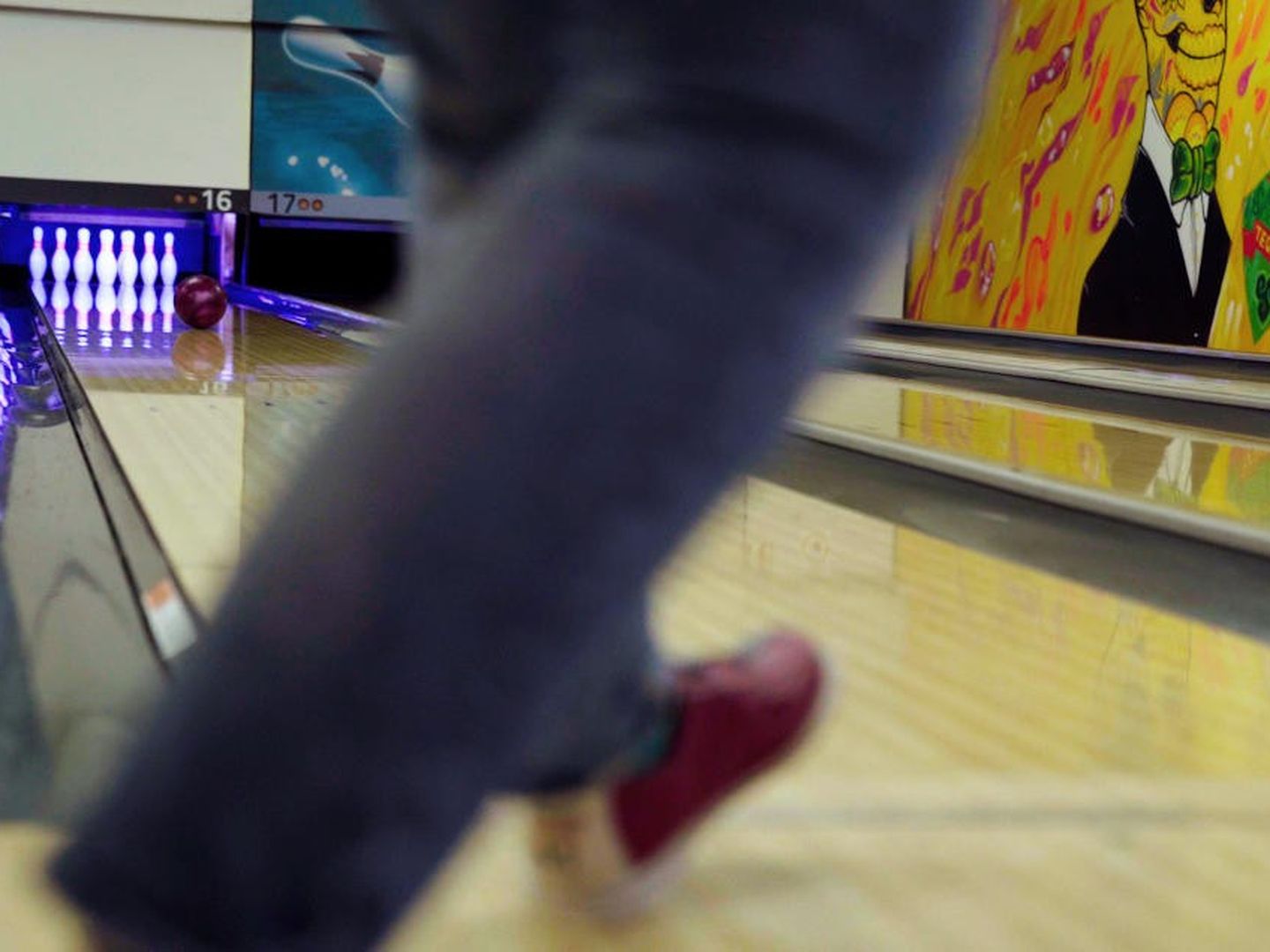 Eine verschwommene Aufnahme zweier Beine in Bewegung am Anfang einer Bowlingbahn.