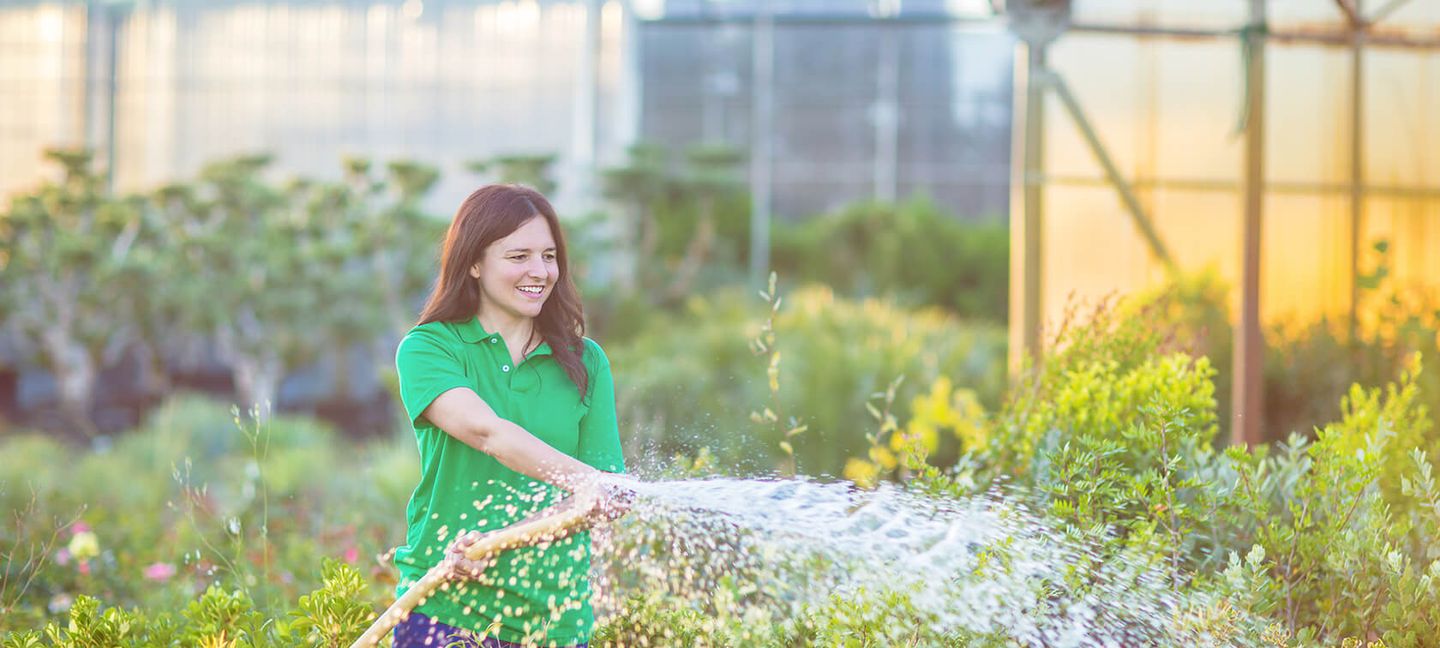 Eine Frau bewässert einen Garten mit einem Schlauch