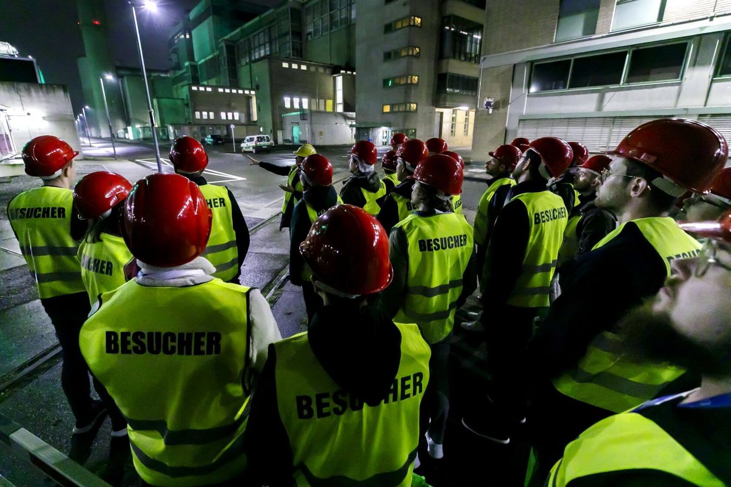 Besucher:innen der Langen Nacht der Industrie stehen als Gruppe samt Warnwesten und Schutzhelmen vor einem Referenten auf Industriegelände. © Stadtwerke Düsseldorf © Stadtwerke Düsseldorf