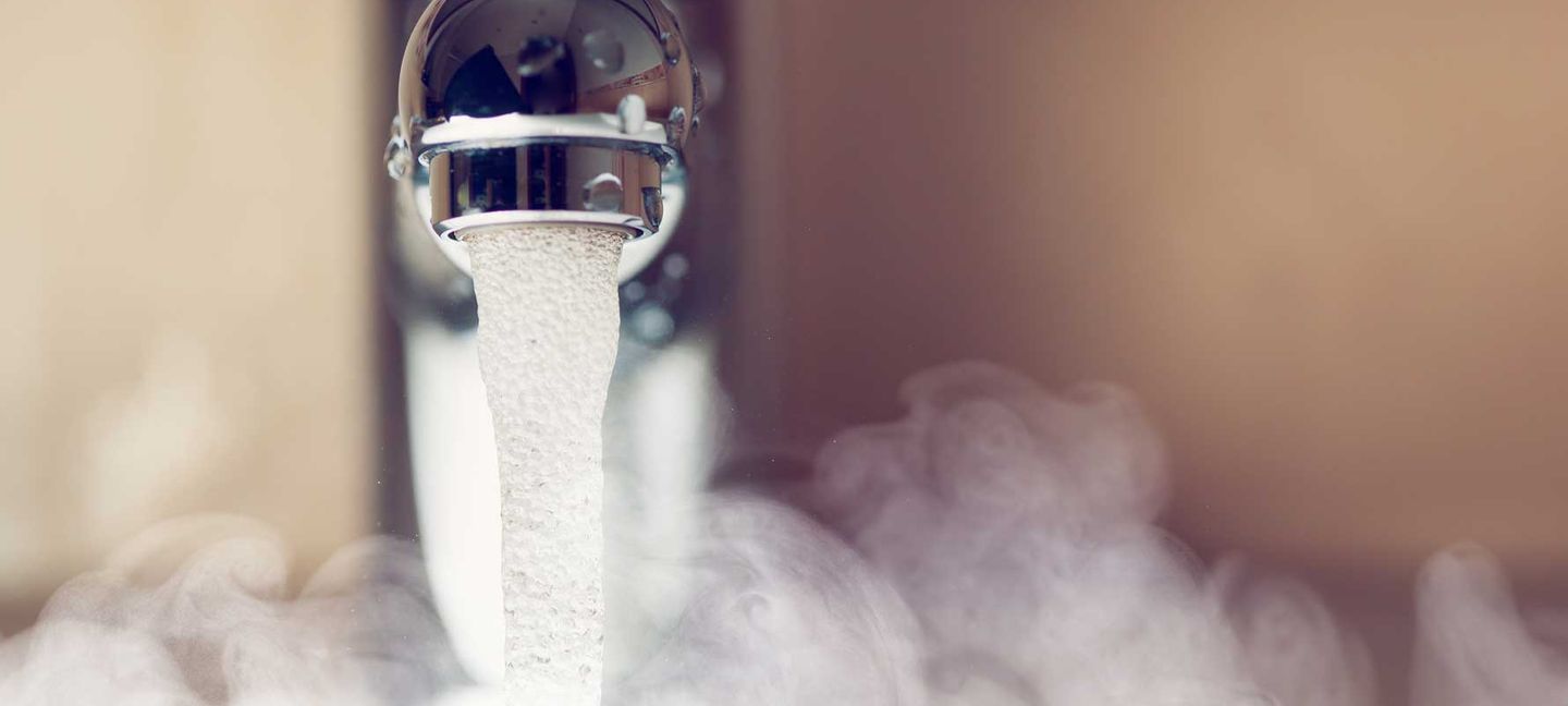 Nahaufnahme eines Wasserhahns, aus dem warmes Wasser fließt, umgeben von aufsteigendem Dampf © nikkytok / iStock / Getty Images Plus via Getty Images