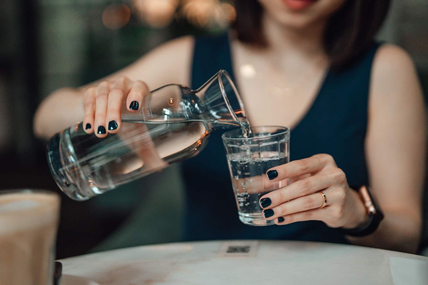 Eine Frau gießt Wasser aus einer Glaskaraffe in ein Trinkglas. Getty