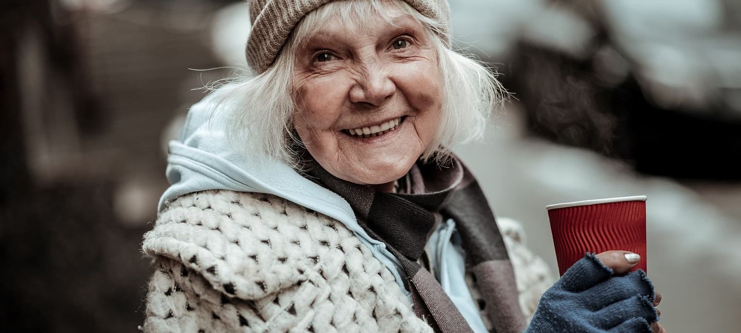 Eine alte Dame mit Becher lächelt in die Kamera