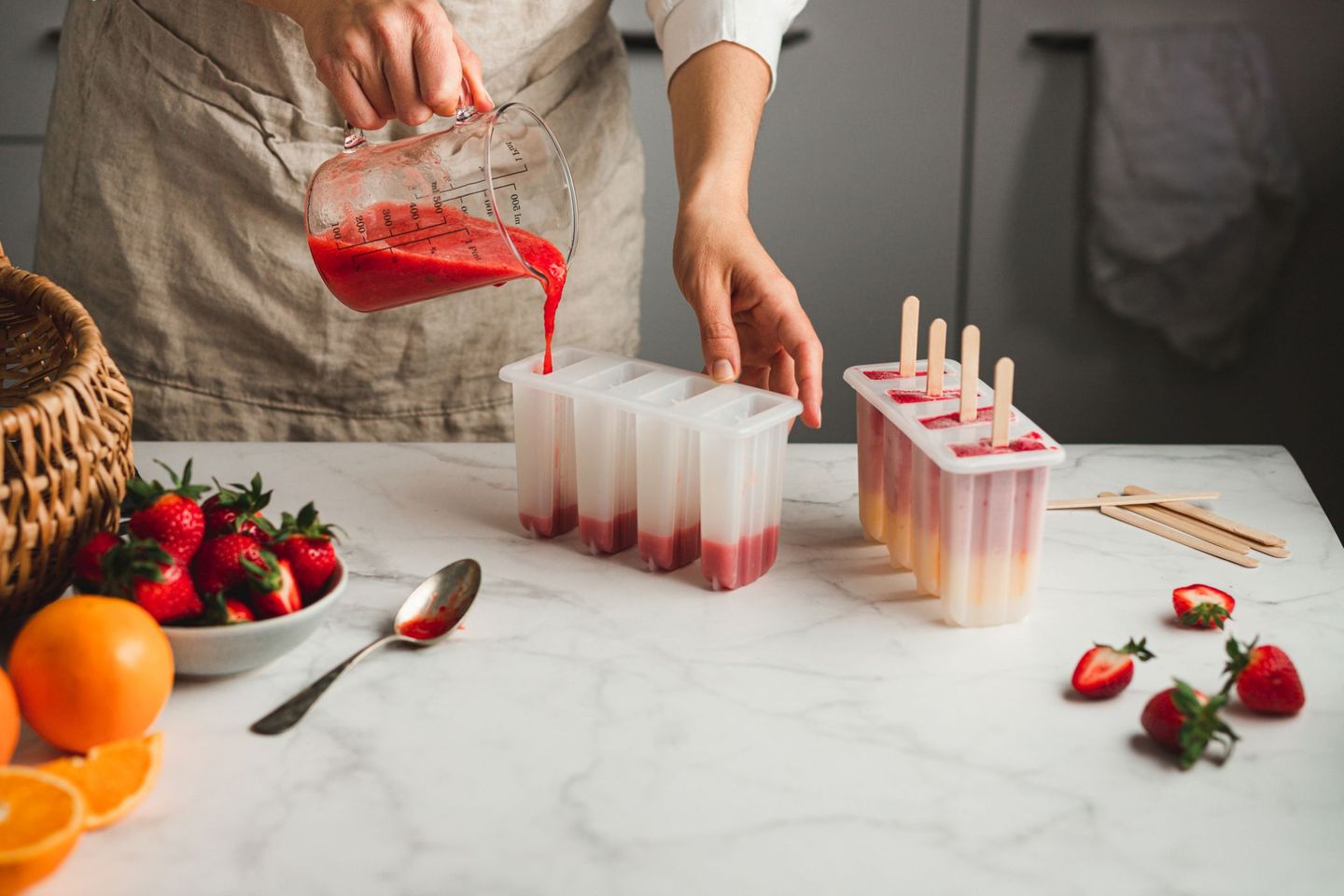 Eine Frau gießt eine rote Fruchtmasse aus einem Messbecher in Eisförmchen. © alvarez / E+ via Getty Images