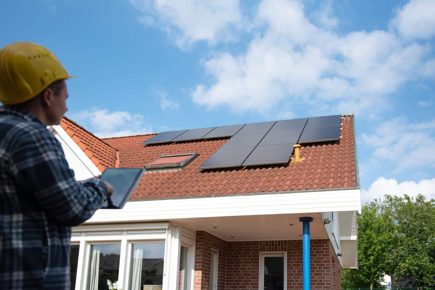 Ein Installateur mit gelbem Schutzhelm steht vor einem Haus, auf dessen Dach Solarmodule installiert wurden. © Nata Dietrich / Moment via Getty Images © Nata Dietrich / Moment via Getty Images