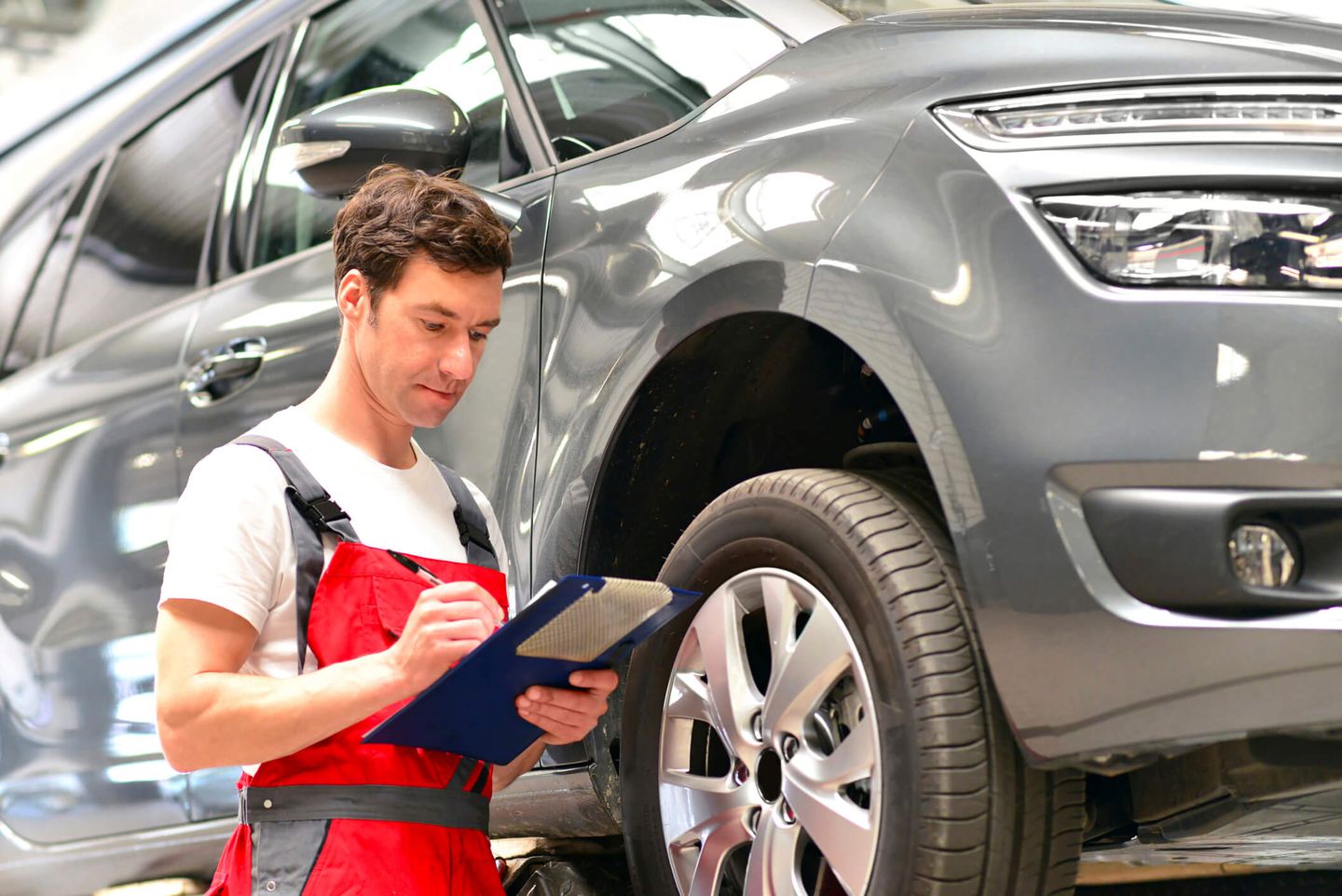 Ein Automechaniker steht neben einem hochgebockten Auto in einer Kfz-Werkstatt. © Westend61 / Westend61 via Getty Images