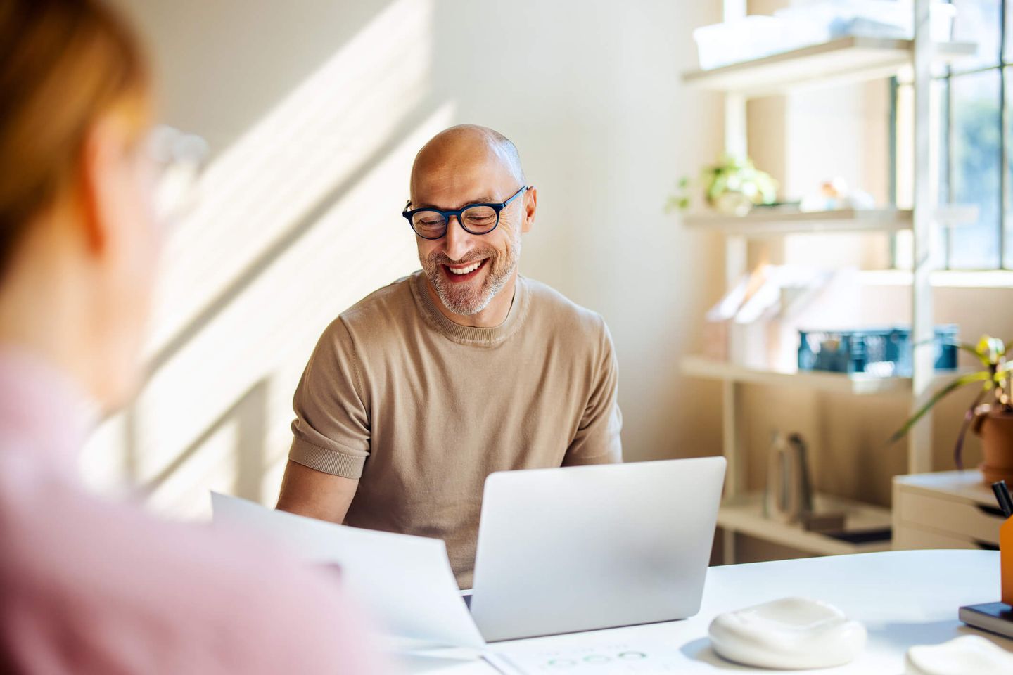 Ein Mann sitzt lächelnd an seinem Schreibtisch. © FreshSplash / iStock / Getty Images Plus via Getty Images