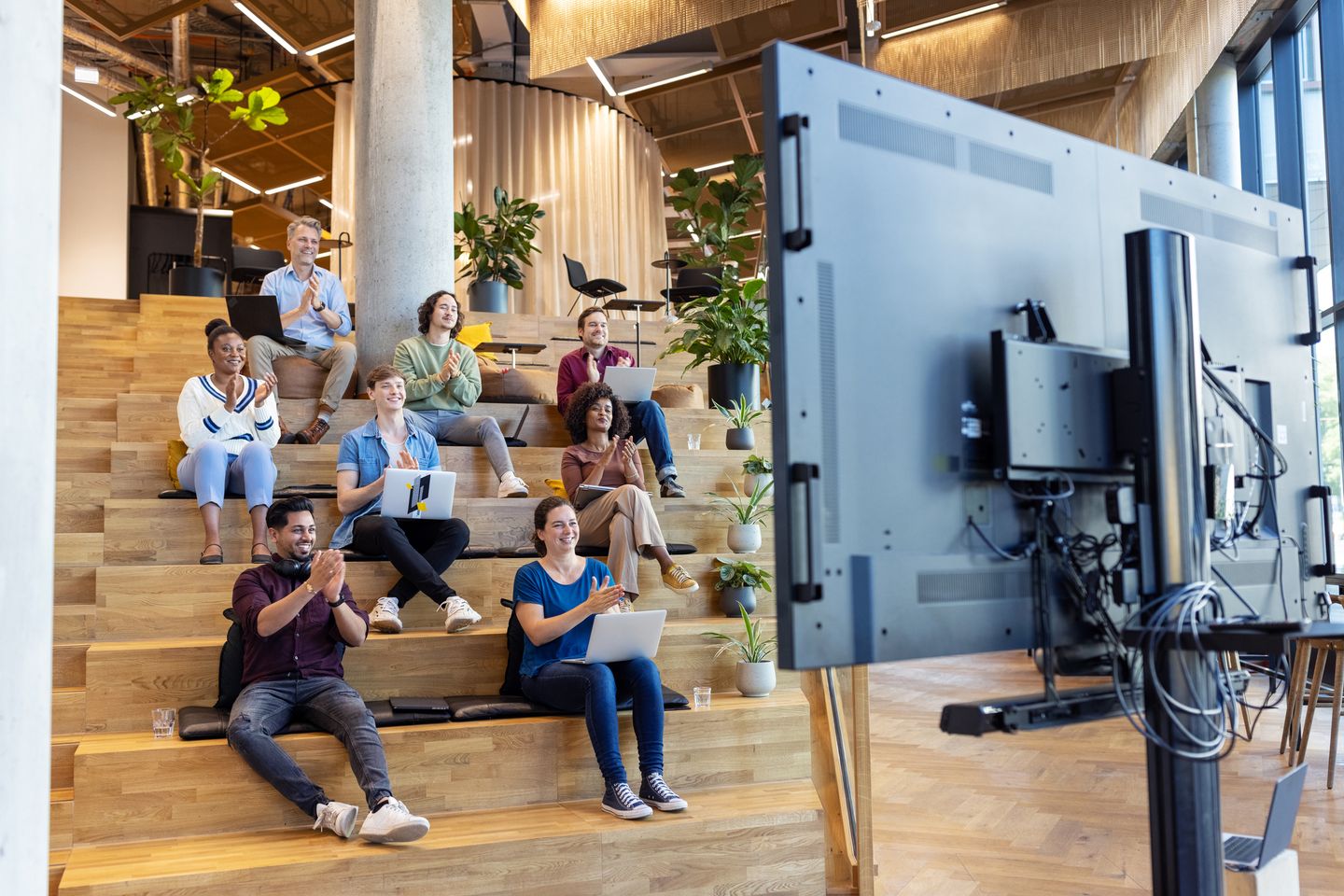 Businessteam sitzt auf Stufen und applaudiert nach einer Videokonferenz. © alvarez / E+ via Getty Images