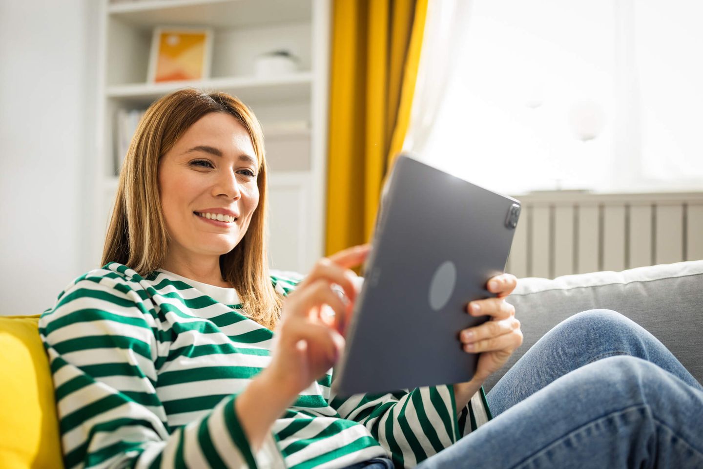 24-Stunden-Lieferantenwechsel: Eine glückliche Frau sitzt auf dem Sofa und bedient ihr Tablet.