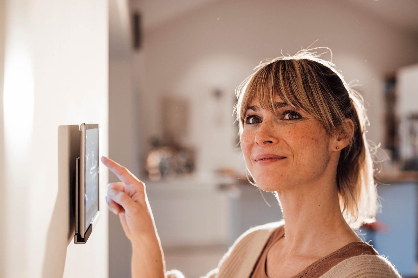 Eine junge Frau nutzt ein Smart Home-System über ein Tablet an der Wand in ihrem Zuhause. © Westend61 / Westend61 via Getty Images