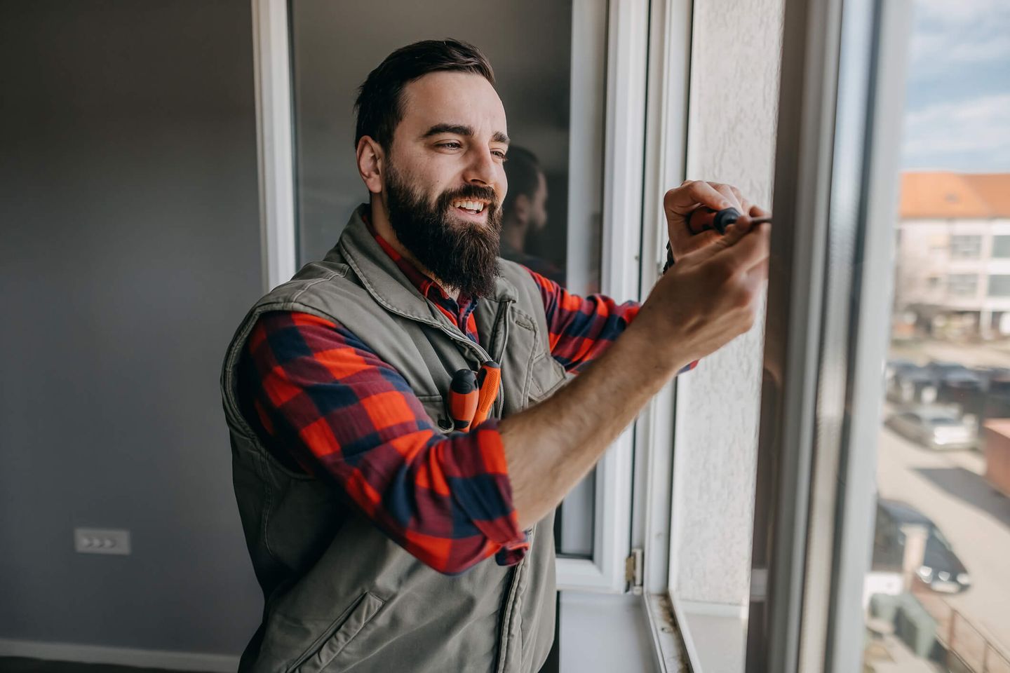 Ein fröhlicher Handwerker schraubt an einem Fenster © enigma_images / E+ via Getty Images