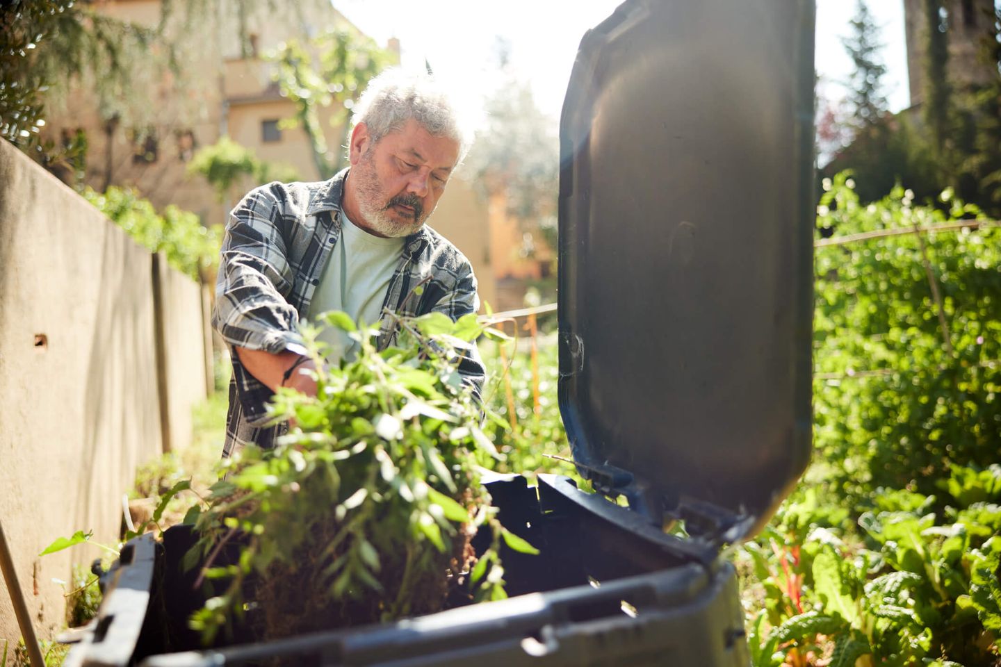 Ein Mann wirft Gartenabfälle in die Biotonne.