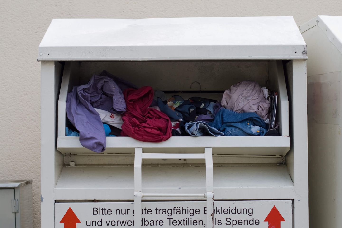 Weißer Altkleidercontainer gefüllt mit Kleidung © HarryHuber / iStock via Getty Images  © HarryHuber / iStock via Getty Images