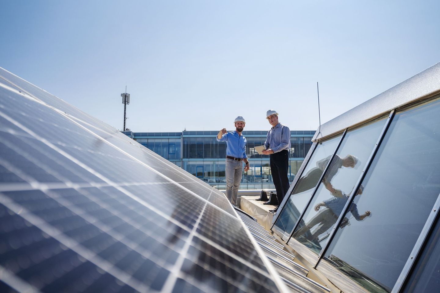 Zwei Ingenieure stehen auf dem Dach eines modernen Gebäudes und inspizieren eine Solaranlage bei sonnigem Wetter. © Westend61 / Westend61 via Getty Images
