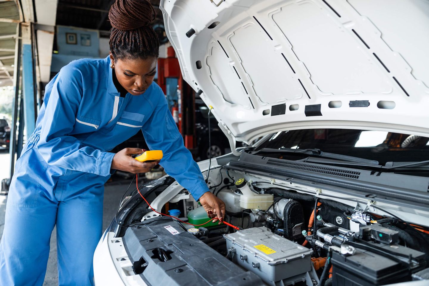 Eine Frau in blauem Overall wartet ein E-Auto, dessen Motorhaube geöffnet ist. © panaya chittaratlert / E+ via Getty Images