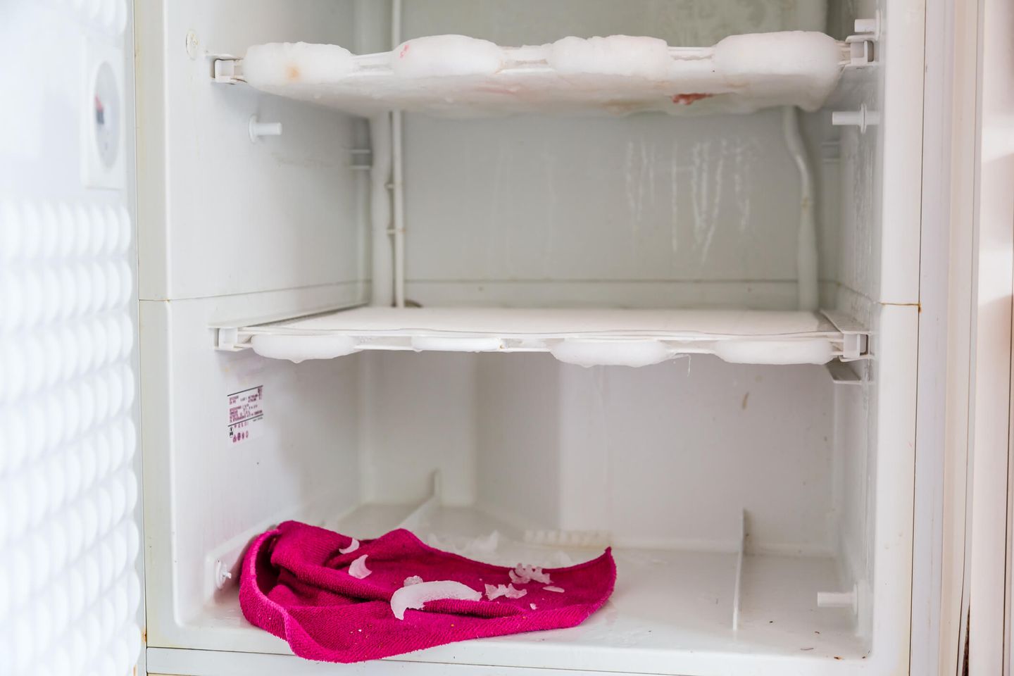 Ein pinkes Mikrofasertuch liegt in einem Gefrierschrank, der gerade bei offener Tür abgetaut wird. © Santiago Urquijo / Moment via Getty Images