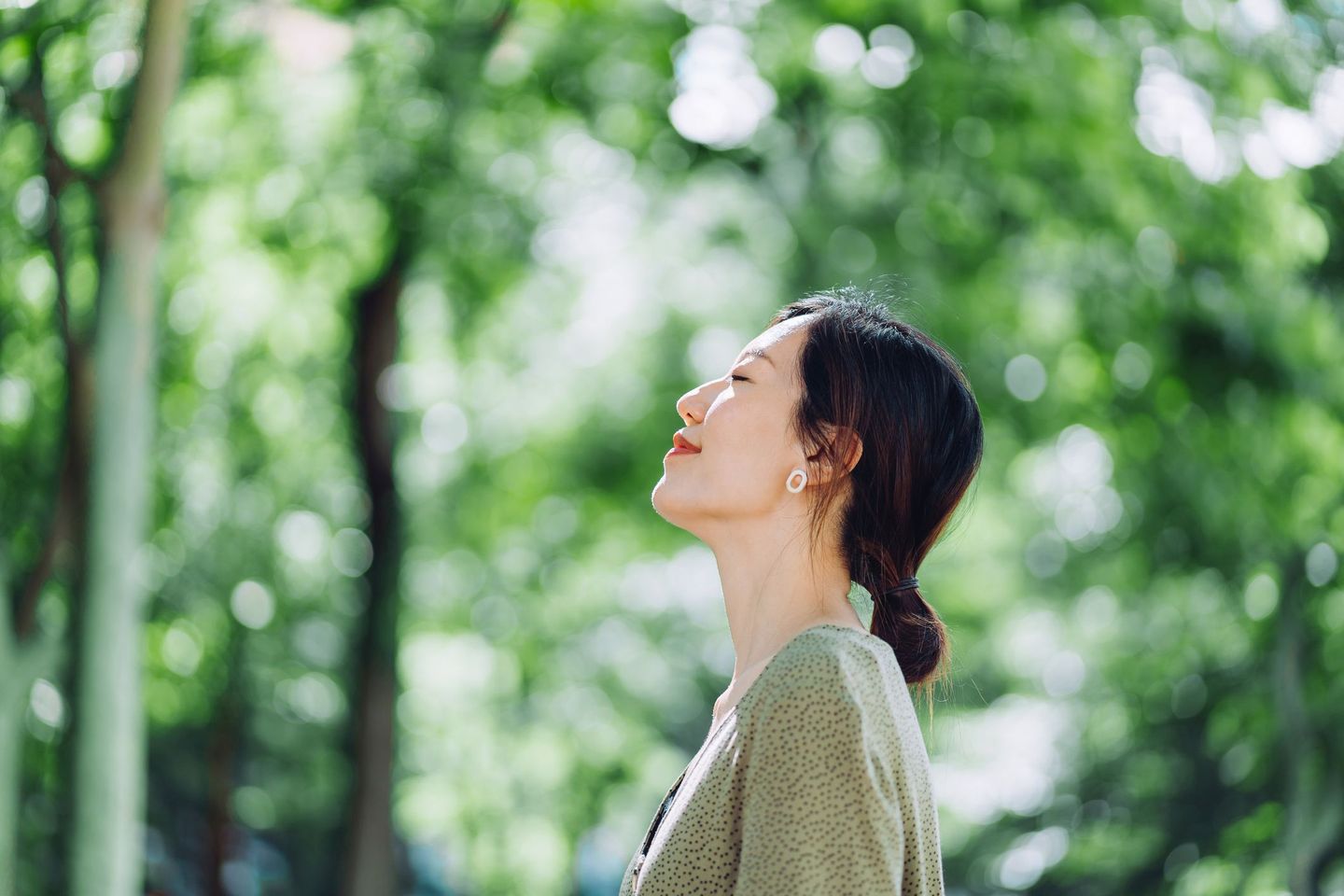 Eine Frau steht mit geschlossenen Augen in einem Wald und genießt die frische Luft. © d3sign / Moment via Getty Images © d3sign / Moment via Getty Images
