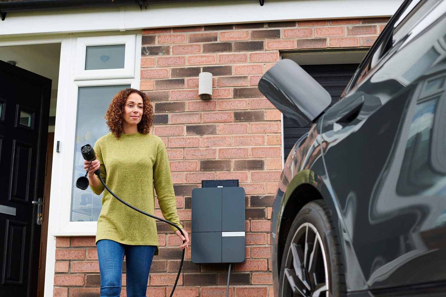 Eine junge Frau auf dem Weg, ihr E-Auto an eine private Ladestation anzuschließen. © sturti / E+ via Getty Images © sturti / E+ via Getty Images