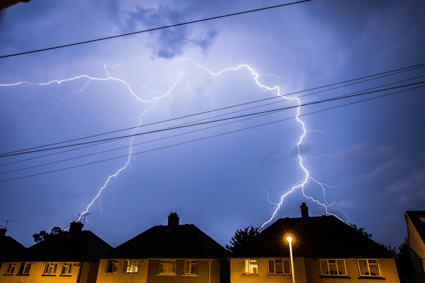 Mehrere Blitze an einem dunklen Wolkenhimmel über Häuserdächern. © Jonathan Beckett / iStock / Getty Images Plus via Getty Images © Jonathan Beckett / iStock / Getty Images Plus via Getty Images