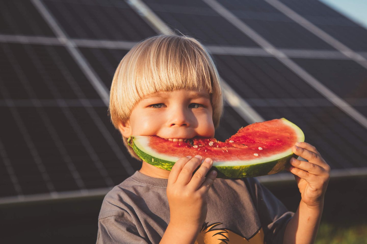 Ein kleiner Junge mit einer Wassermelone und Sonnenkollektoren im Hintergrund. © Iuliia Bondar / Moment via Getty Images