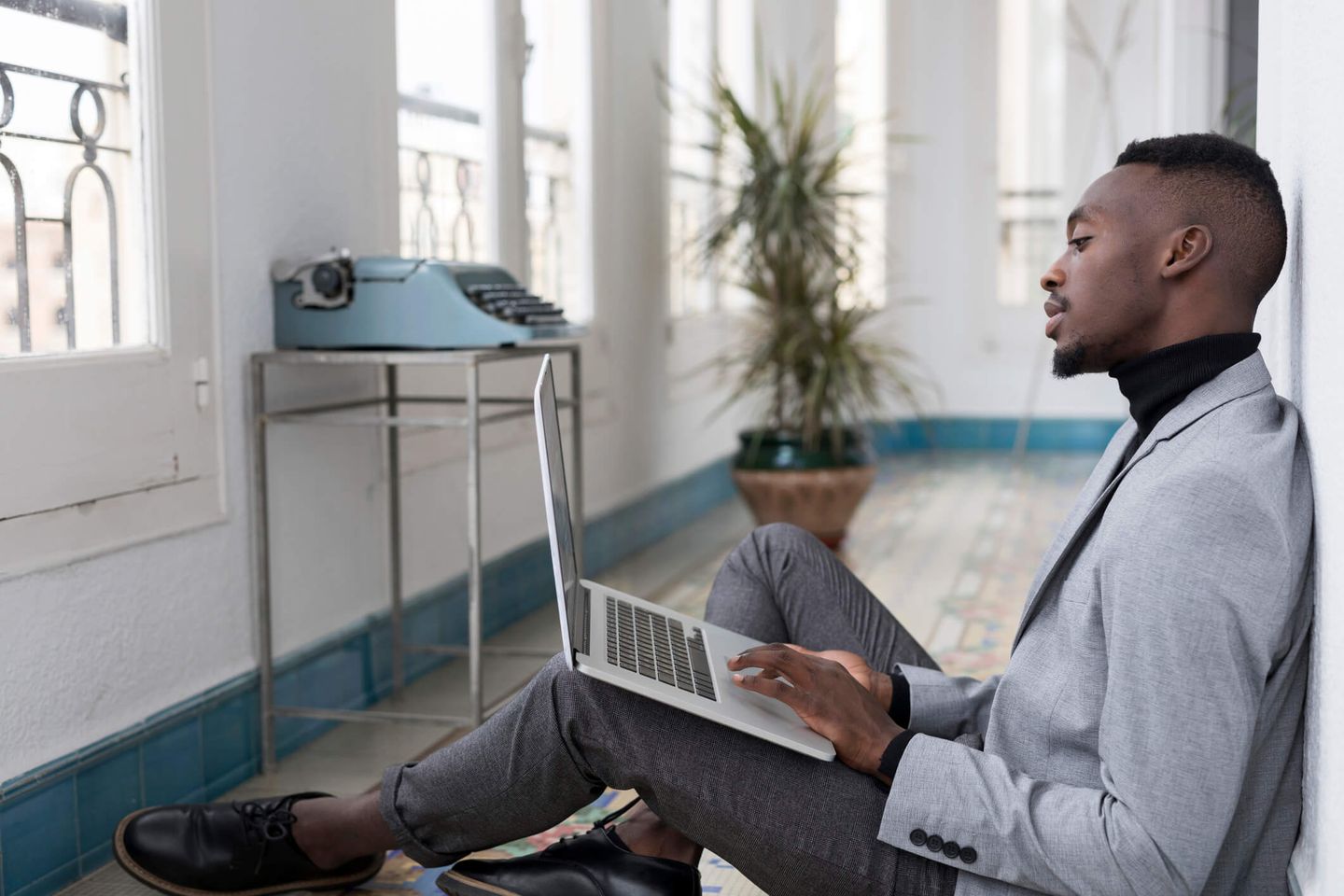 Ein Mann sitzt mit einem Laptop auf dem Schoß auf dem Boden. © Westend61 / Westend61 via Getty Images