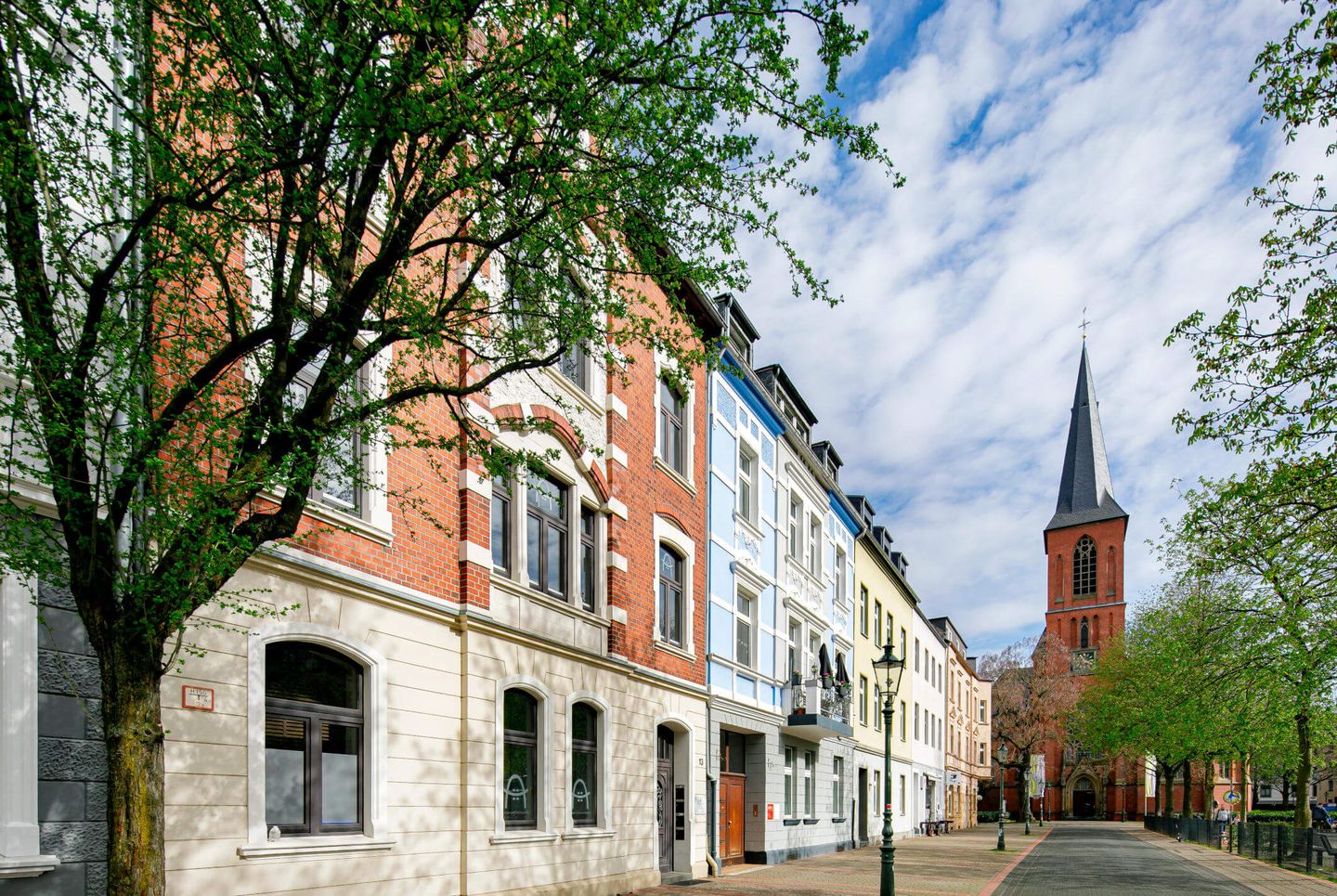 Eine Häuserreihe in Düsseldorf Eller und die Gertrudiskirche im Hintergrund.