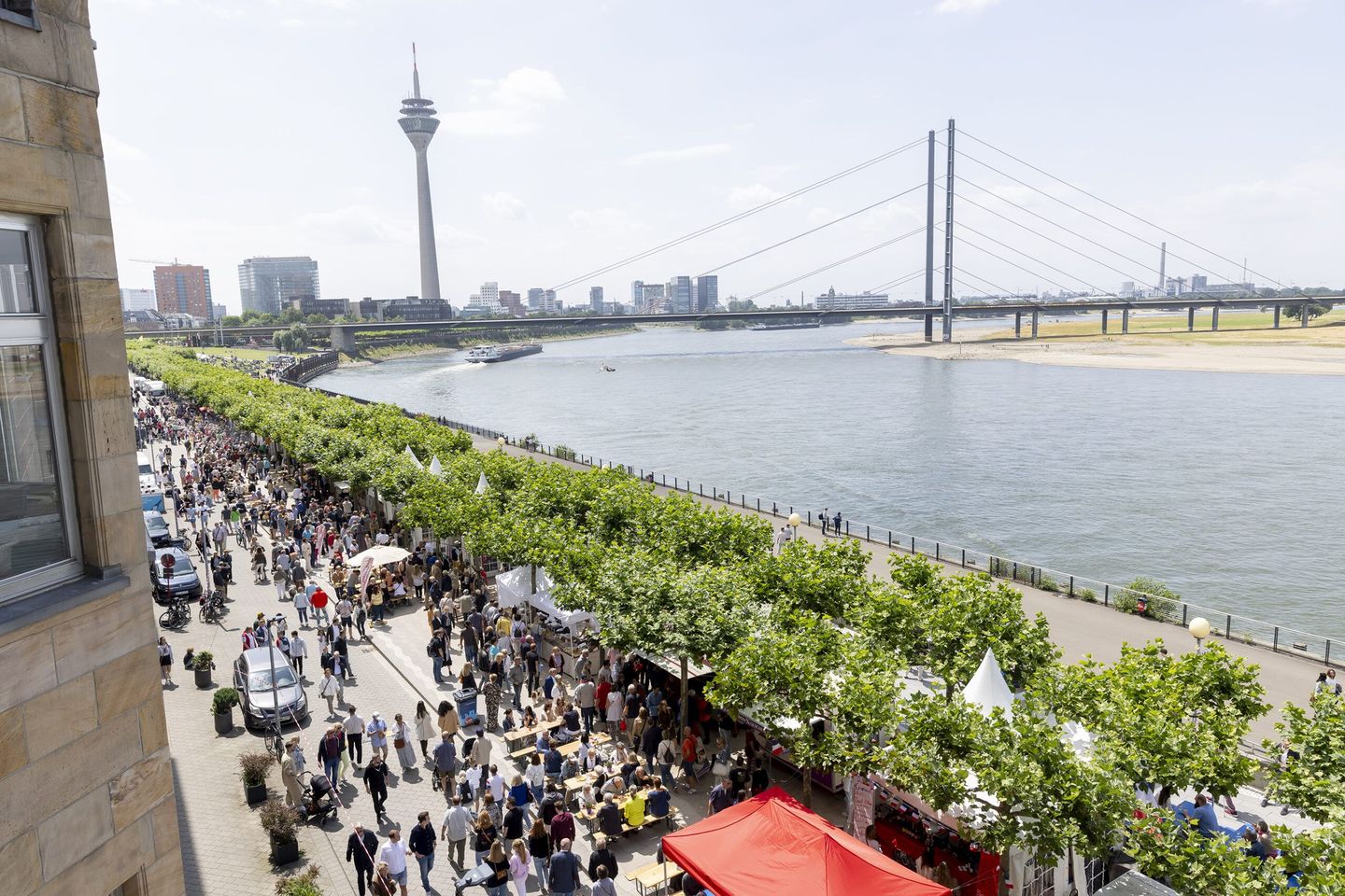 Die gut besuchte Rheinuferpromenade Düsseldorf im Vorder- und der Rheinturm im Hintergrund. © Destination Düsseldorf Veranstaltungs GmbH / Wellfairs GmbH via www.duesseldorfer-frankreich-fest.de