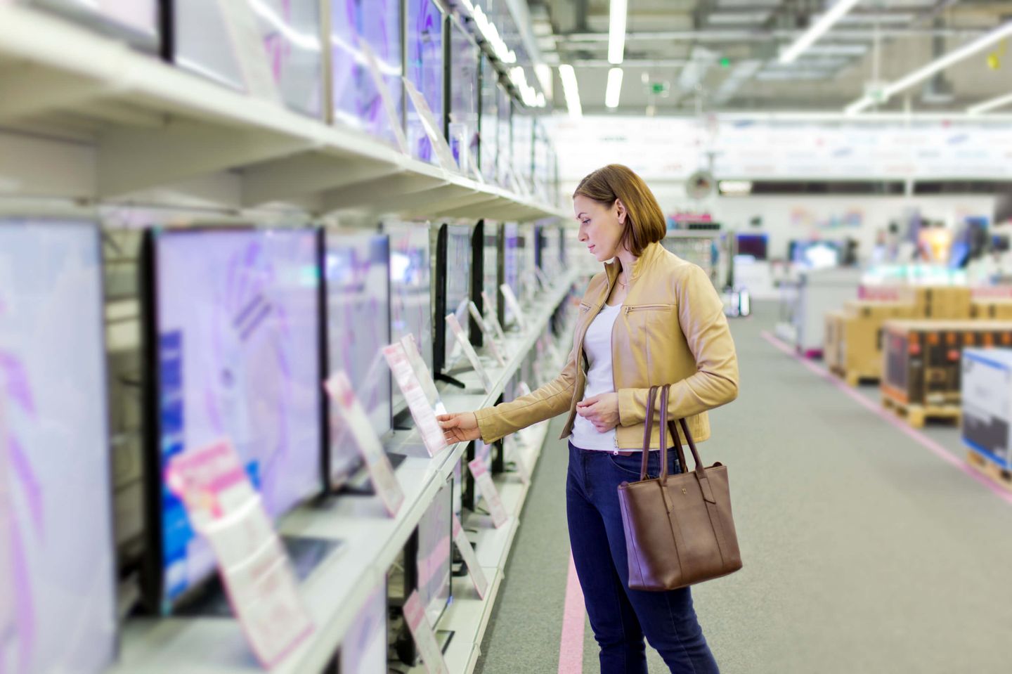 Frau vergleicht Fernseher in einem Elektronikgeschäft.