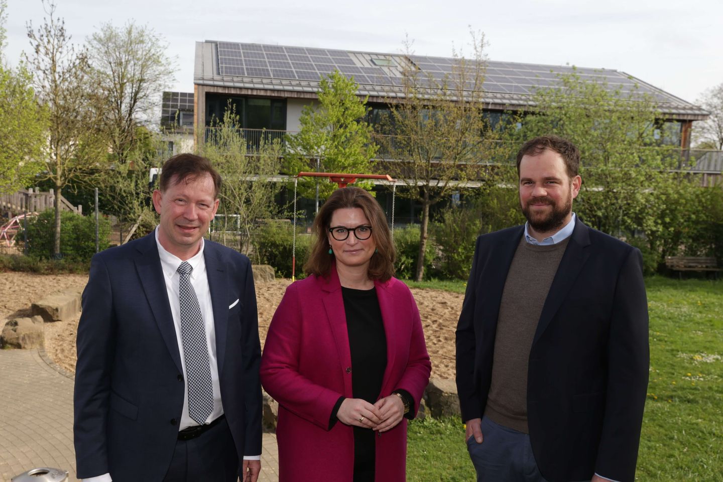 Die Projektverantwortlichen stehen vor einer Schule mit Photovoltaikanlagen.