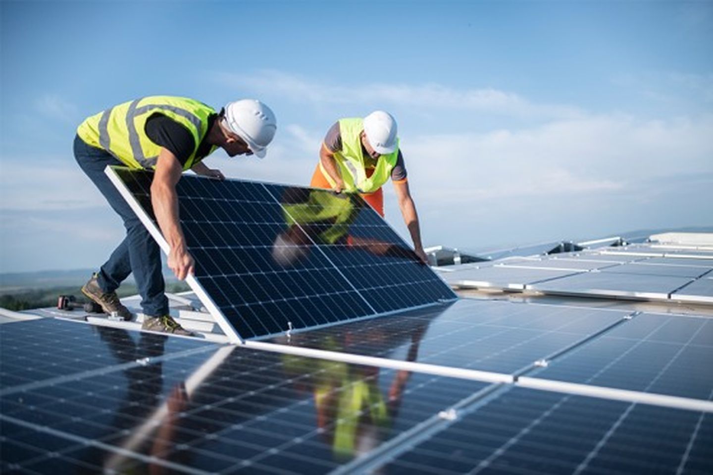 Zwei Installateure bringen Photovoltaik-Sonnenkollektoren auf dem Dach eines Unternehmens an. © ArtistGNDphotography via via Getty Images
