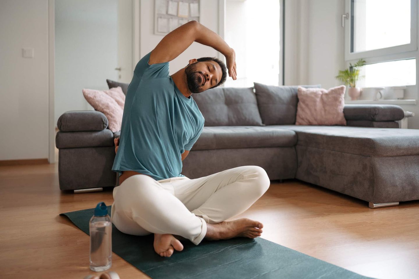 Mann macht seitliche Dehnübung im Wohnzimmer auf Yogamatte Getty