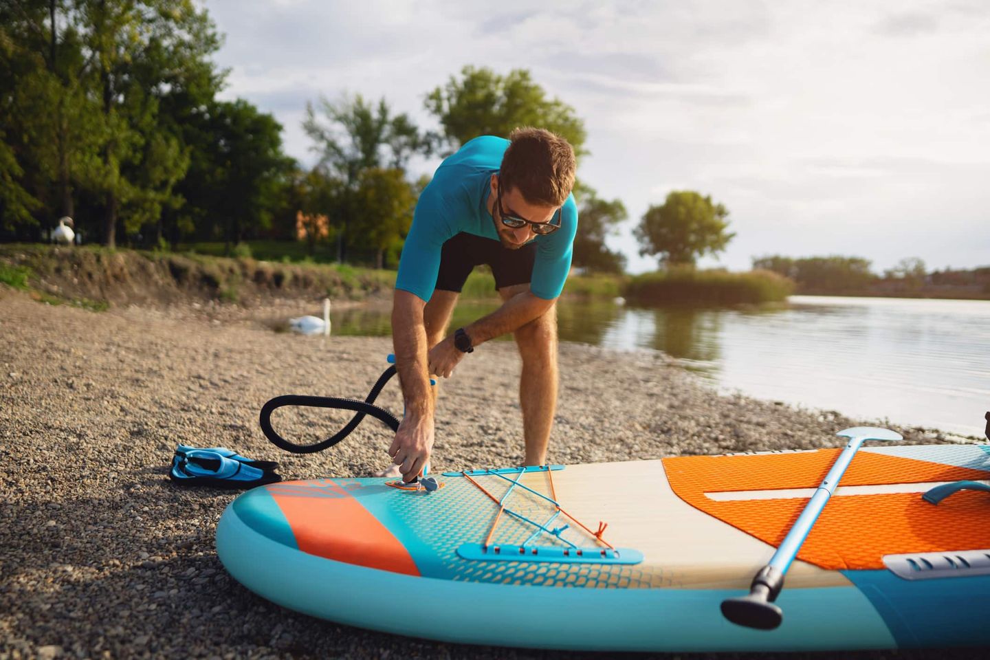 Mann pumpt ein buntes SUP-Board am Ufer eines Sees auf