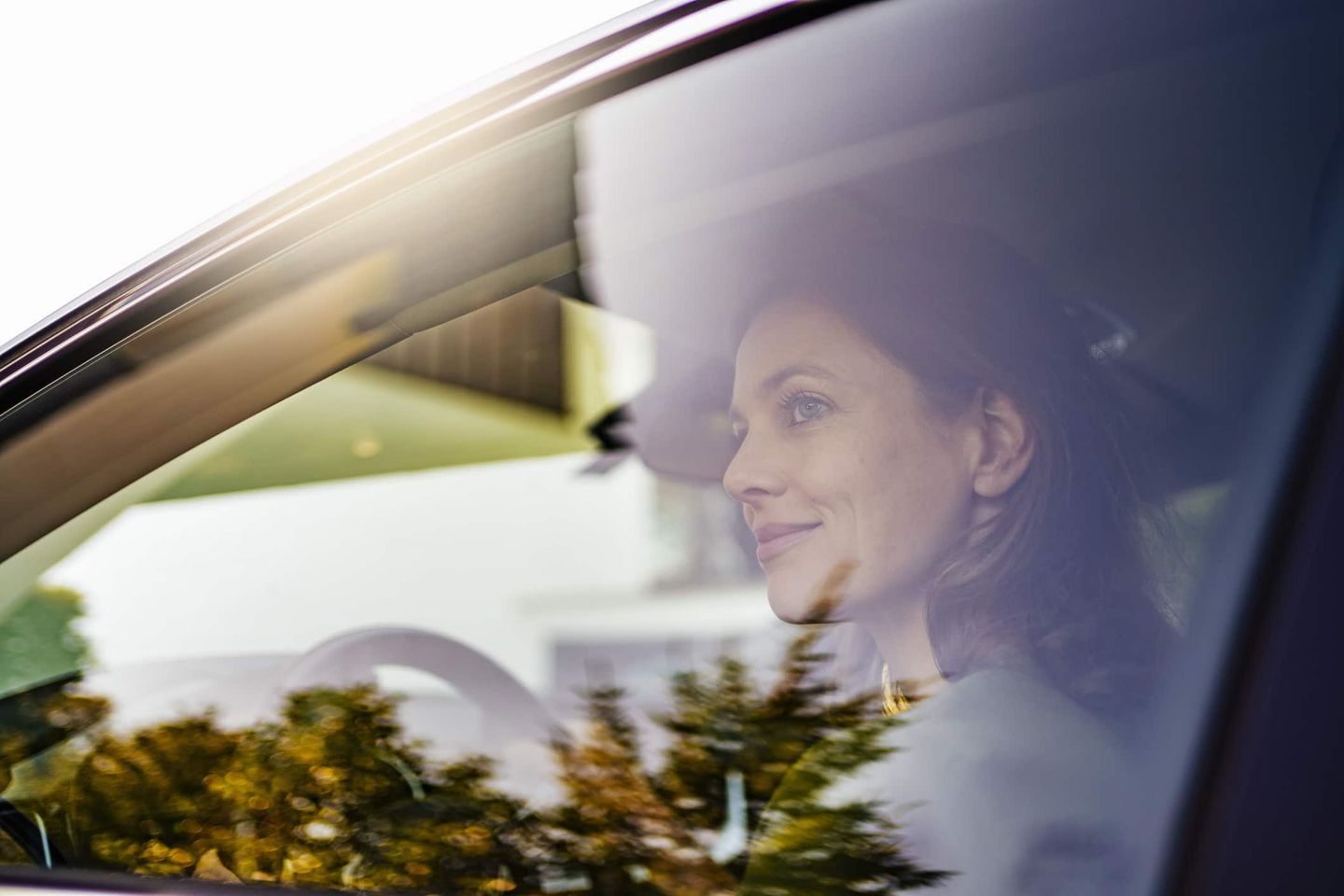 Frau sitzt lächelnd am Steuer eines Autos, gesehen durch die Seitenscheibe. Getty